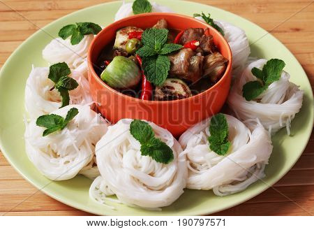 Green curry in an orange cup in the middle of a plate Thai-rice-flour Noodles (kanom jeen)