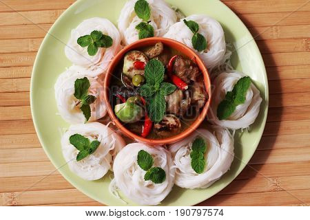 Green curry in an orange cup in the middle of a plate Thai-rice-flour Noodles (kanom jeen)