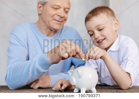 Sharing life wisdom. Clever handsome mature guy teaching his grandson about some basic economic principles while illustrating his speech with vivid examples