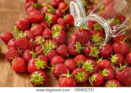 Fresh red strawberries for jam in a glass jar on the brown wooden table. Many strawberries in the glass jar and on the table. Horizontal photo. Seasonal fruits. Food backgrounds and still-life. Concept of the vitamin food.