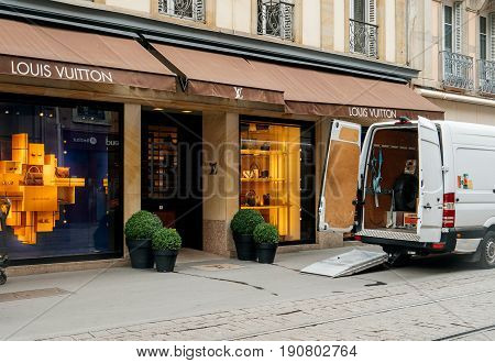 STRASBOURG FRANCE - JUN 12 2017: Wite delivery van suppling stock with clothes parcels and accesories a windows of the Louis Vuitton store on empthy shopping street