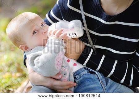 Adorable Baby Drinking Milk From Bottle In Mother Hands