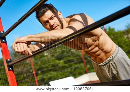 Outdoor portrait of mail bodybuilder, sunlit, looking away.