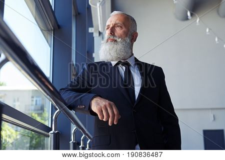 Low angle of concentrated gentleman with grey beard looking out window