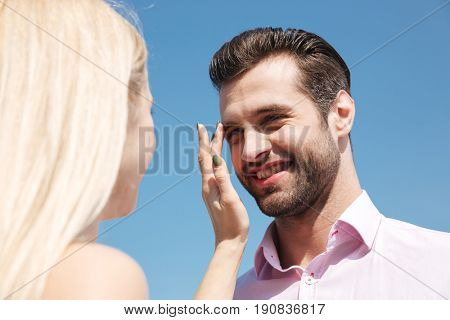 Young handsome cheerful man looking at his blonde woman while walkinf near river on bridge