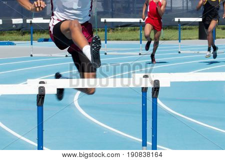 High school boys race in the 499 meter intermediate hurdels on a blue track. Running around the second turn.