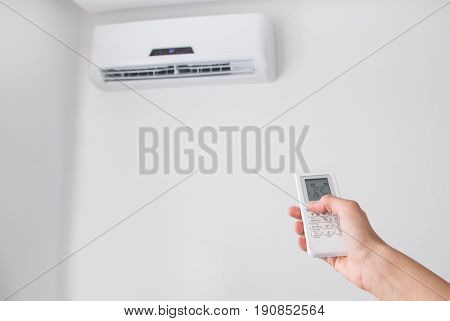 Hand holding remote control, adjusting temperature of air conditioner mounted on a white wall. Indooor comfort temperature