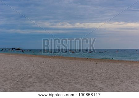Several fishing boats launching from from a South Florida beach near the peir at sunrise on a calm cloudy summer morning.