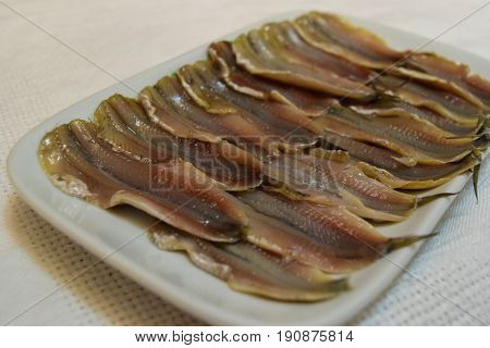 Wizened salty anchovy fish in ceramic plate on white tablecloth background