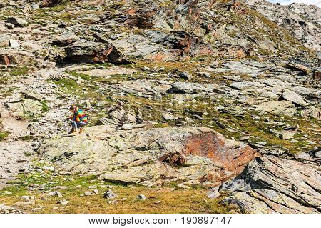 Cute little girl wearing bright rainbow colored coat and beige boots resting in mountains Switzerland