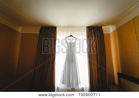 luxury wedding dress hanging on window in a hotel room