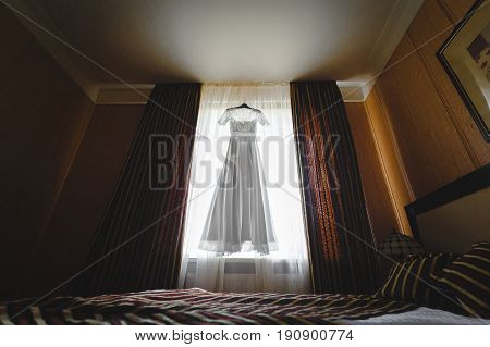 luxury wedding dress hanging on window in a hotel room