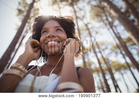 Low angle view of smiling woman listening music against trees