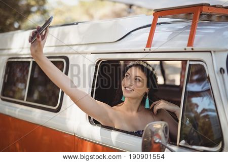 Young woman clicking selfie while sitting in van at forest