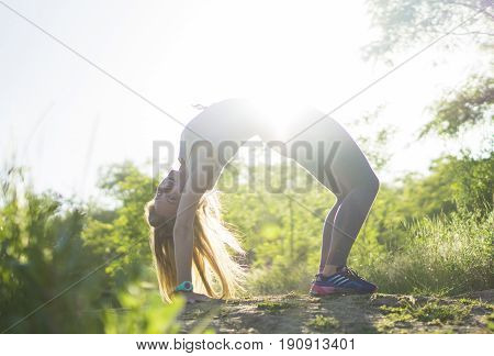 Young woman in gray top practicing yoga in beautiful nature. Stretch workout outdoor evening