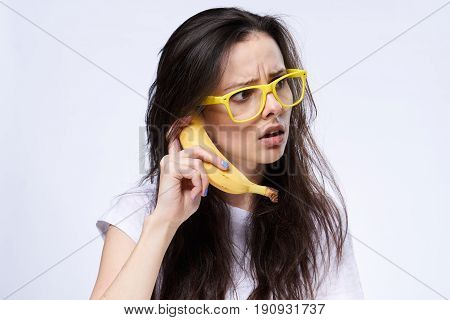 Surprised woman with glasses and a banana on a light background.