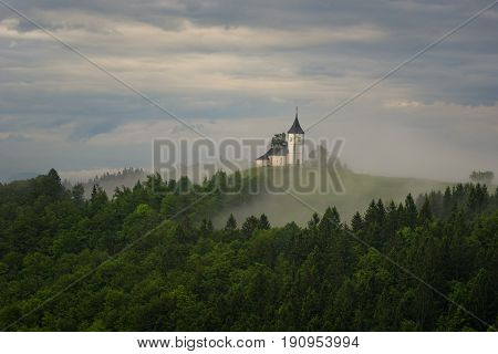 Jamnik church on a hillside in the spring, foggy weather at sunset in Slovenia, Europe. Mountain landscape shortly after spring rain. Slovenian Alps.