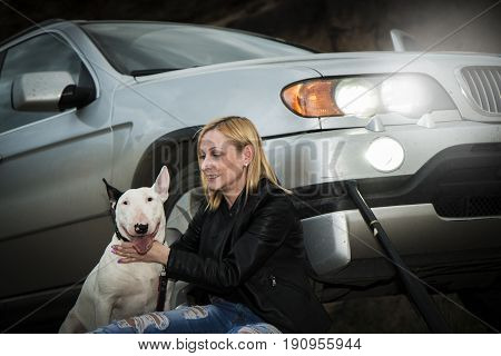 Brutal, daring girl with a fighting dog breed of bull terrier, near his car against the background of the rock