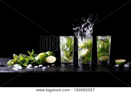 Mojito summer party refreshing tropical cocktail non alcohol drink in highball glass with splash soda water, lime juice, mint leaves, sugar, ice and rum. Dark black background with copy space text
