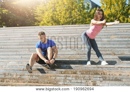 Fit fitness woman and man doing stretching exercises outdoors at park. Couple doing hamstring leg stretching exercise and stretches. Female amd male sports models exercising outdoor in summer.