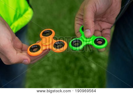 trendy fidget spinner - two persons holding green and orange fidget spinners in hands, close up view