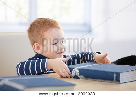 ¿Jengibre pelo niño mirando enciclopedia en mesa, sonriendo.?