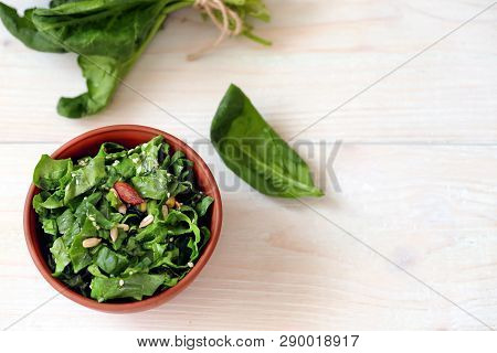 Spinach Salad With Seeds, Nuts And Sunflower Oil In Pottery On A Light Wooden Background With Space 