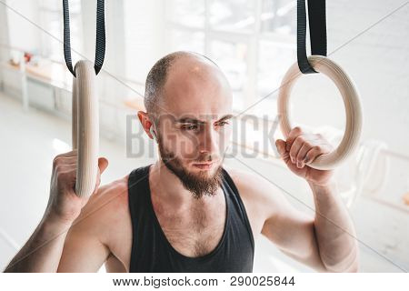 Strong Bearded Athlete With Wireless Headphone Holding Crosstraining Rings At Hall. Muscular Man Hol