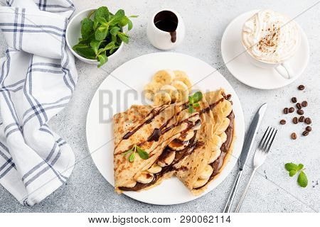 Crepes With Banana, Chocolate And Cup Of Cappucino On Concrete Background. Top View Sweet Breakfast 
