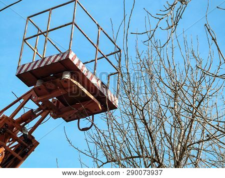 Empty Aerial Work Platform In The Air Against The Blue Sky And Bare Tree Branches, Close-up. The Con