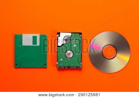 Data Storage Medium Evolution - Floppy Disk, Cd Disk, Small Hard Disk Drive On Orange Background. To