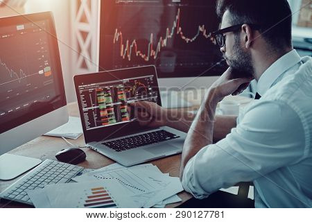Concentraiting On Project. Rear View Of Young Businessman In Formalwear Analyzing Data Using Compute