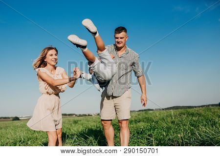 Mother And Father Swinging Son In Sunnny Summer Day