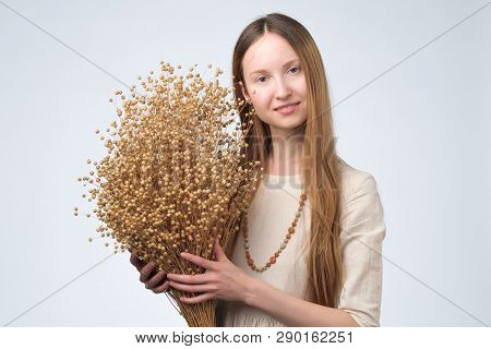 Beautiful European Woman With Long Hair Holding Bouquet Of Dry Flowers Of Flax.