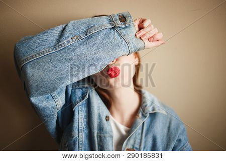 Young Anonymous Woman In Denim Jacket Covering Her Face With Her Hand And Showing Kiss Gesture