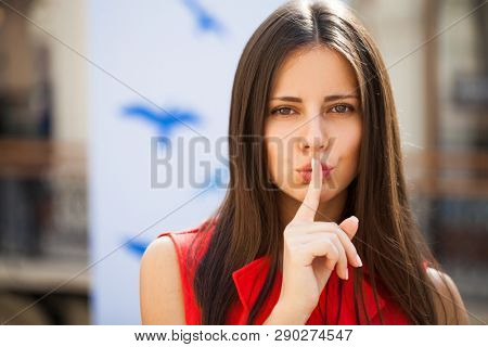 Woman requires silence. Young beautiful brunette girl has put forefinger to lips as sign of silence, isolated on white background