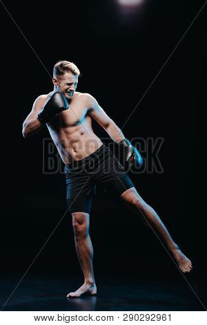 Front View Of Muscular Barefoot Strenuous Boxer In Boxing Gloves Doing Kick On Black