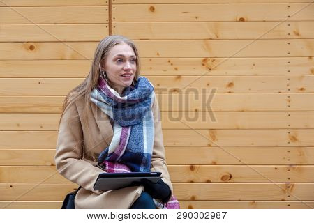 Blonde Beautiful Woman Holding Tablet Outdoor. Portrait Of Young Woman Wearing Tartan Scarf In Front