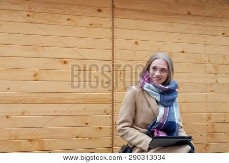 Blonde Beautiful Woman Holding Tablet Outdoor. Portrait Of Young Woman Wearing Tartan Scarf In Front