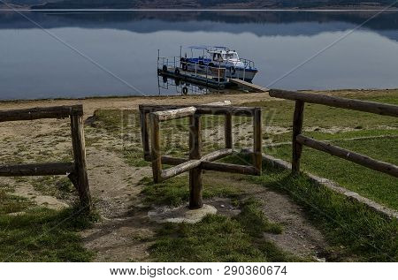 Panorama Of Batak Dam Reservoir With Passenger-ship In The Water, Coastal Autumn Glade And Wooden Fe