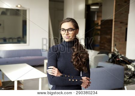 Attractive Young Woman Looking Thoughtfully And Smiling While Standing Indoor