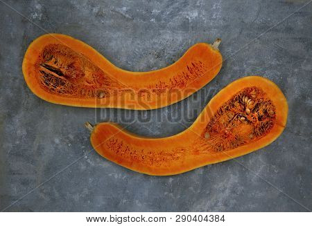 Two Halves Of The Pear-shaped Pumpkin Are Located On The Concrete Horizontally Close To Each Other.