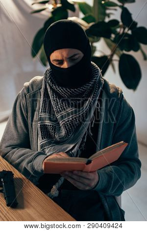 Serious Terrorist In Black Mask Reading Book At Table