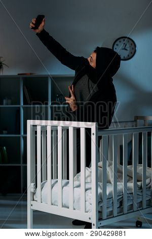 Criminal In Mask Taking Selfie Near Crib And Showing Peace Sign