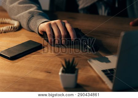 Partial View Of Criminal With Gun And Smartphone On Wooden Table