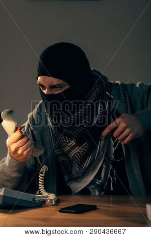 Angry Criminal In Mask Aiming Gun And Looking At Handset