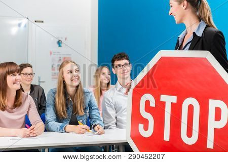 Driving instructor holding theoretical part of driving lessons with stop sign in her hand