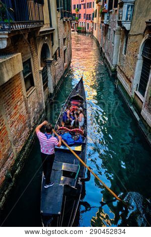 VENICE, ITALY - JUNE 27, 2018: Narrow canal between colorful old houses with gondola boat with tourists and gonolier in Venice, Italy