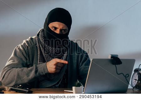 Terrorist In Mask Looking At Webcam And Pointing With Finger At Laptop Screen