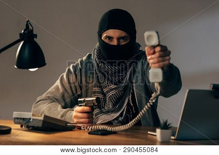 Angry Terrorist In Black Mask Holding Gun And Showing Handset At Camera